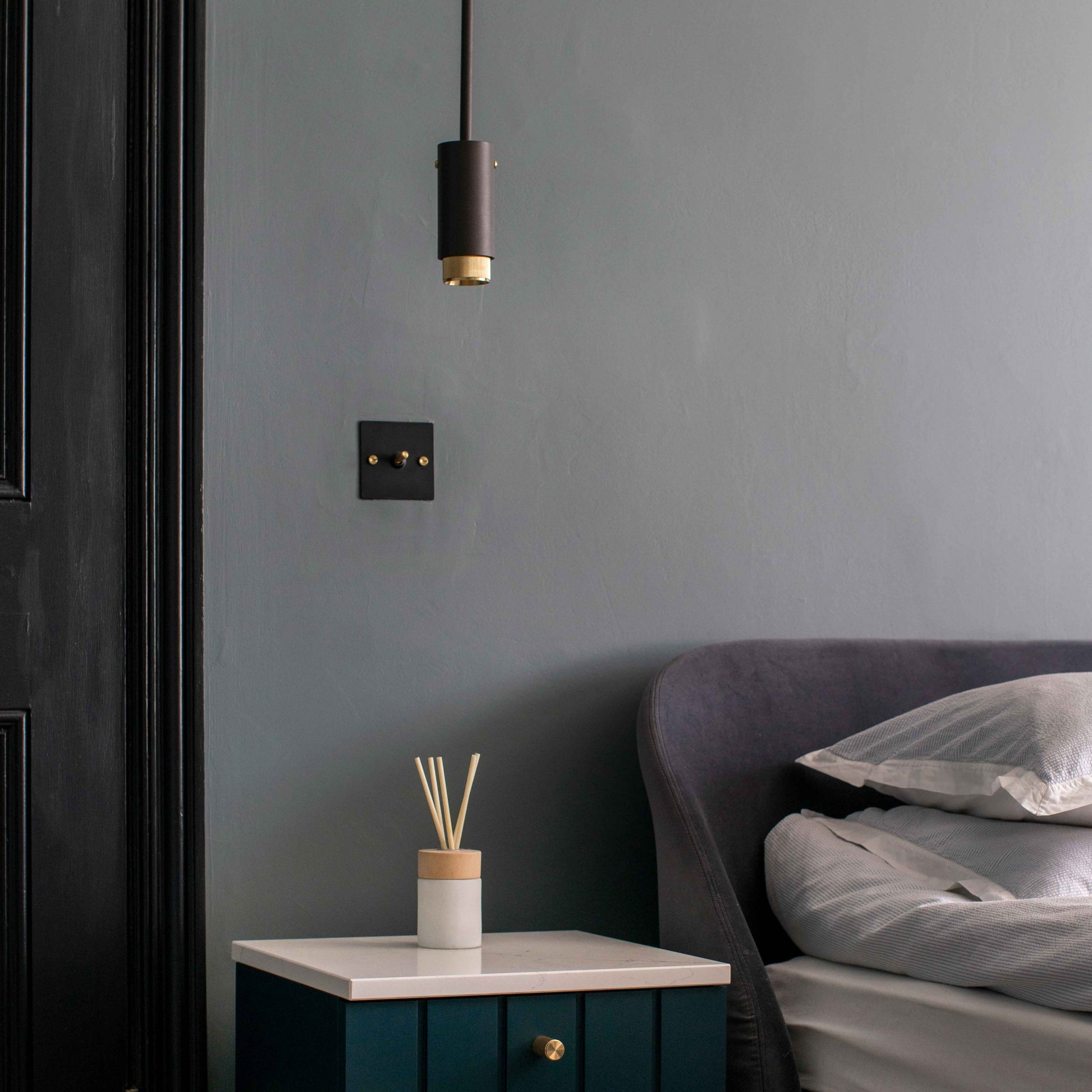 Exhaust Pendant Light / Linear / Graphite Brass, in setting hanging from ceiling above bedside table in bedroom.